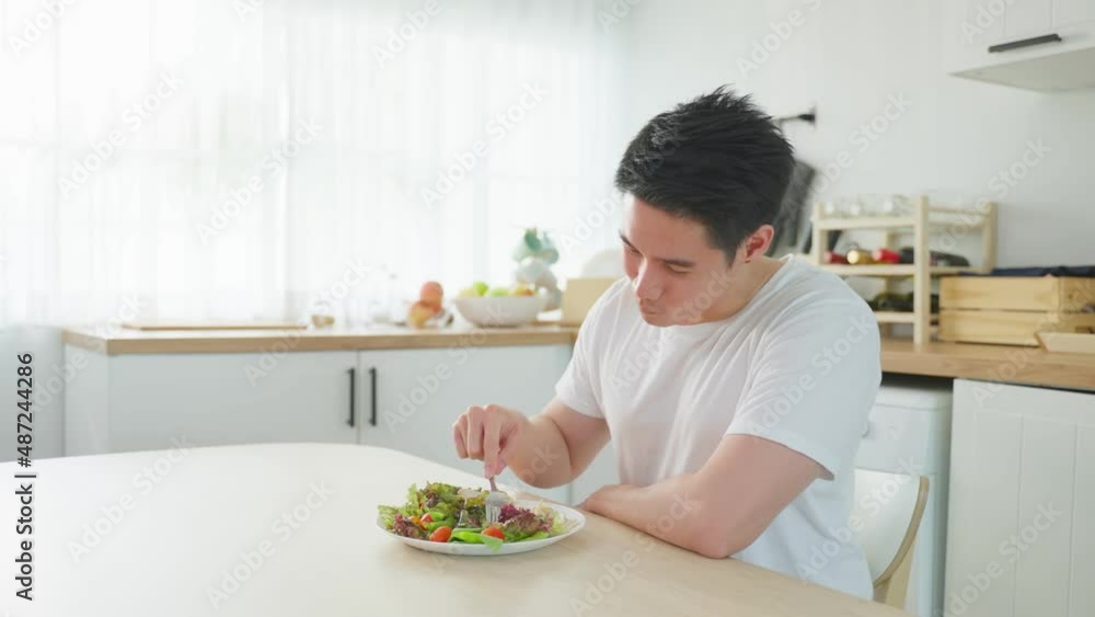 Asian attractive handsome male eating green salad in kitchen at home. Asian attractive handsome male eating green salad in kitchen at home.