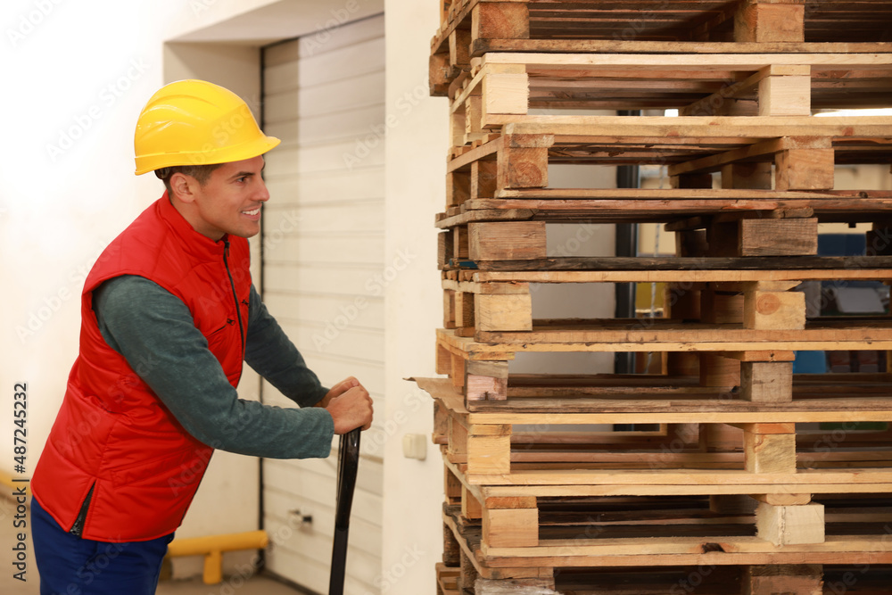 Worker moving wooden pallets with manual forklift in warehouse Worker moving wooden pallets with manual forklift in warehouse