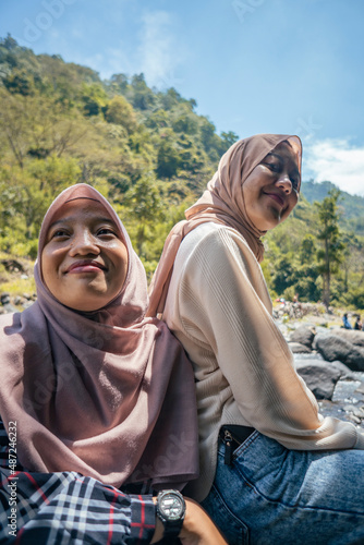 Two Indonesian girl smiling pose when she got on the top of mountain and down river valley. the photo perfect for family holidays background, nature pamphlet and advertising brochure.
