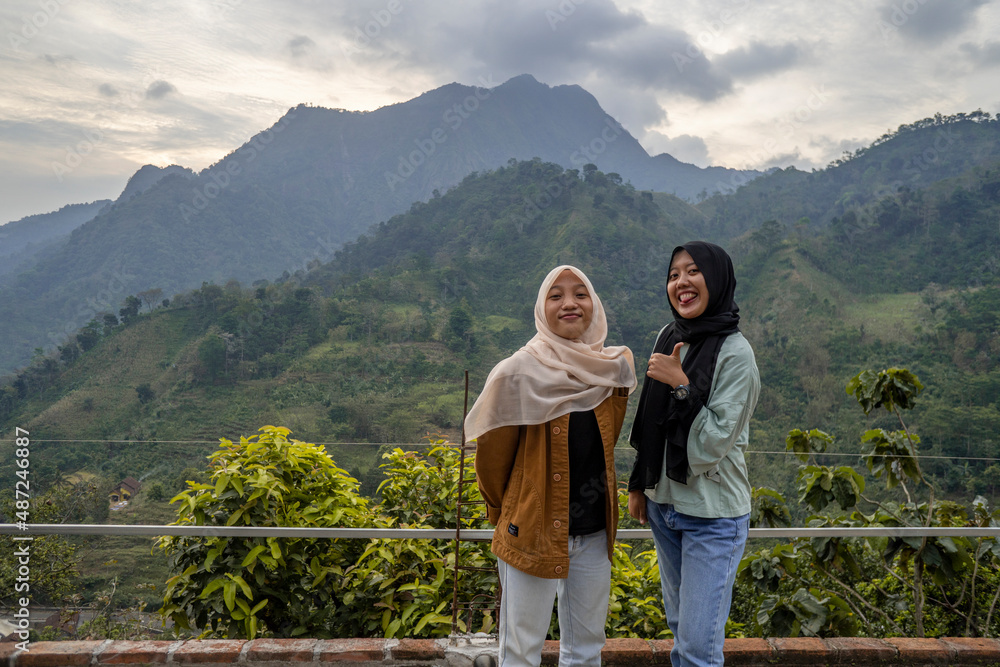 Two Indonesian girl smiling pose when she got on the top of mountain. the photo perfect for family holidays background, nature pamphlet and advertising brochure.