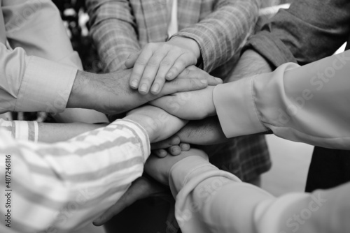 People holding hands together in office, closeup. Black and white effect