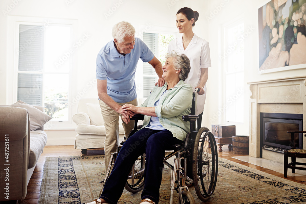 The life of a senior. Shot of a smiling caregiver with a senior woman in a wheelchair and her husband at home. The life of a senior. Shot of a smiling caregiver with a senior woman in a wheelchair and her husband at home.