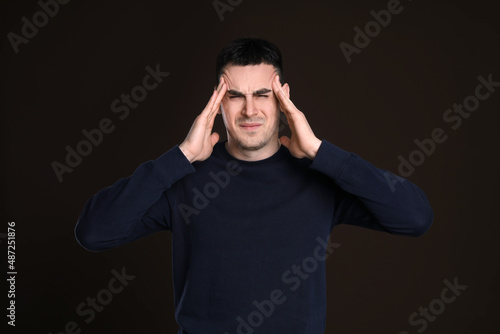 Young man suffering from headache on dark background. Cold symptoms