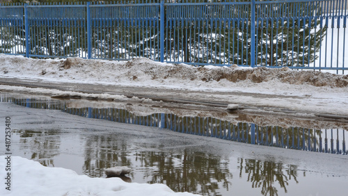 A road with melting snow, puddles and ice on a cloudy spring day. Reflections in cold water. Snow and mud. Thawed patches. Spring has come, the month of March.