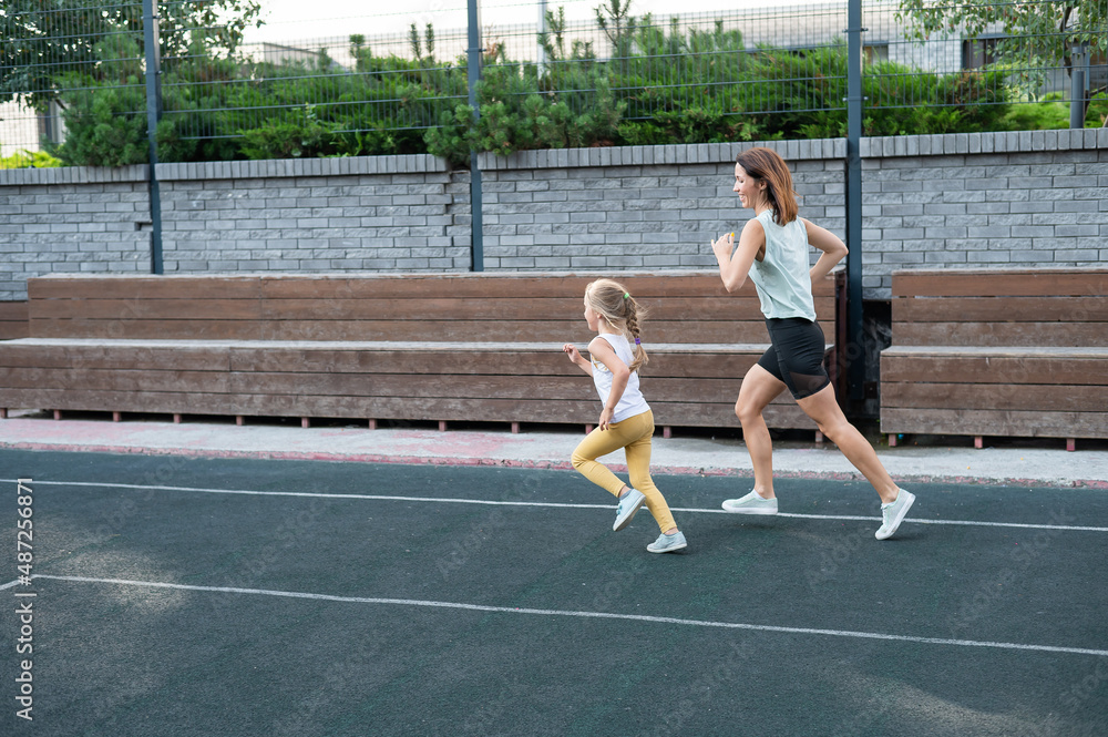 Obraz premium Caucasian woman goes in for sports with her daughter outdoors. A schoolgirl and her mother are running around in the stadium.