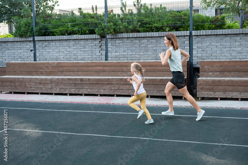 Caucasian woman goes in for sports with her daughter outdoors. A schoolgirl and her mother are running around in the stadium.