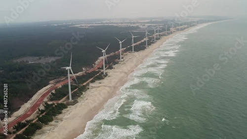Array of onshore horizontal axis wind turbines located on a long beach coastline with high ocean swell on a cloudy day. Hainan island, China photo