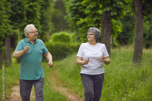 Happy healthy senior couple enjoying jogging workout in nature. Energetic old husband and wife looking at each other as they are running along green park path. Sport  fitness  active lifestyle concept