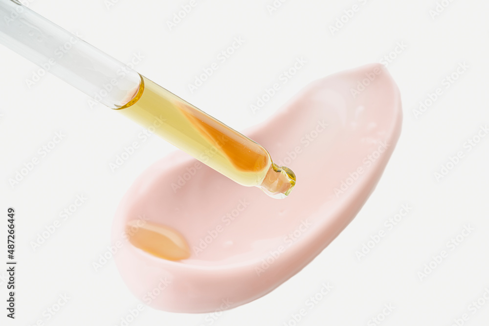 Cosmetic pipette with drops of oil, on the background of pink cosmetic cream smear. Cosmetic pipette with drops of oil, on the background of pink cosmetic cream smear.