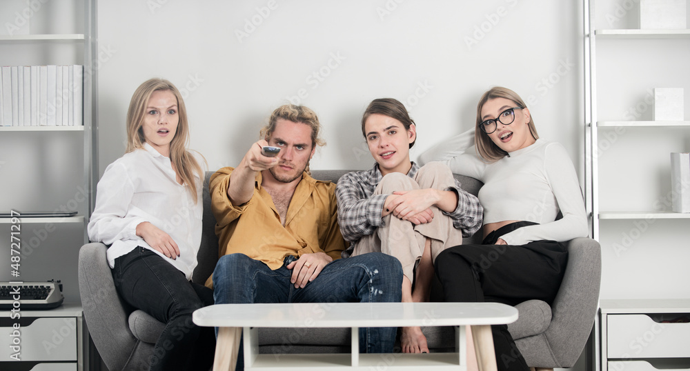Youth group. Friends watching TV in evening at home. Group of young people sitting on sofa and talking at home. Young attractive people watch movies at home.