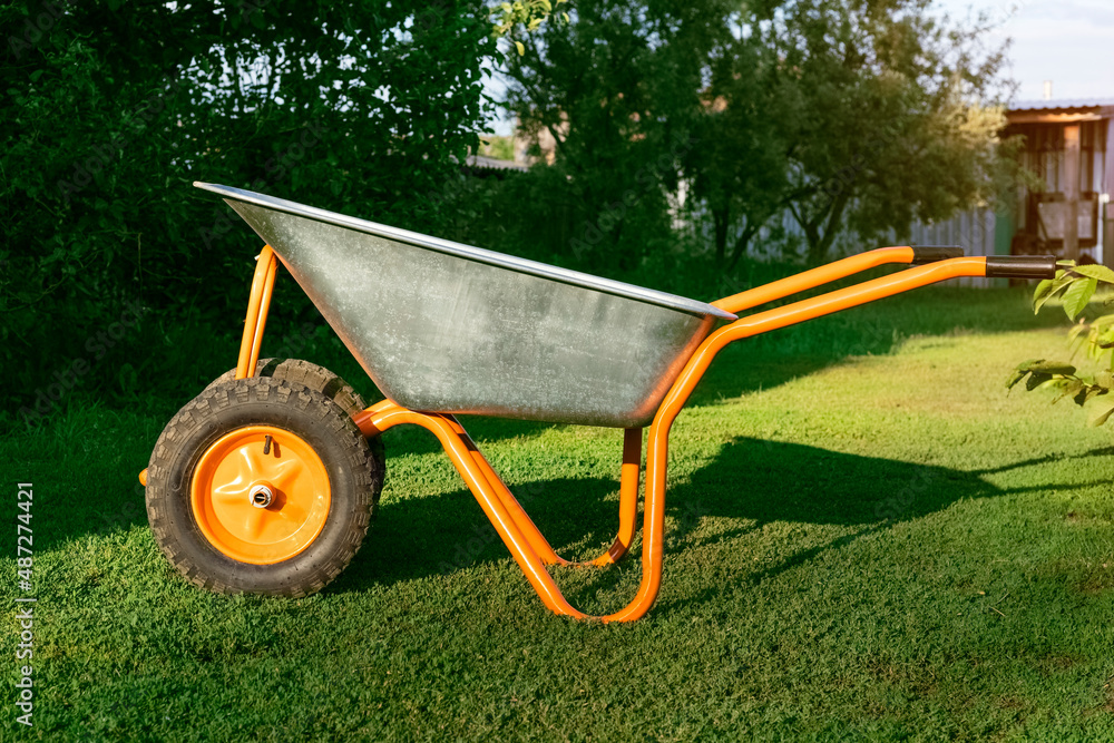 Fototapeta premium Garden cart, wheelbarrow in a green garden. Cleaning season of the garden area, park or preparing the garden for planting