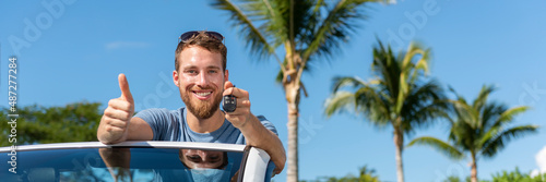 Car key new young owner driver man showing keys and thumbs up happy for new convertible buy or sell used cars. Driver's license concept with driving cabriolet on road trip banner panoramic.