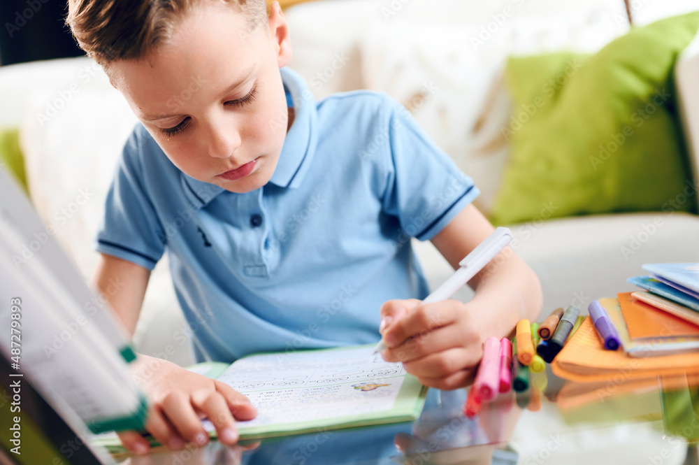 Thinking child bored, little boy writing carefully sitting at desk and doing homework Thinking child bored, little boy writing carefully sitting at desk and doing homework
