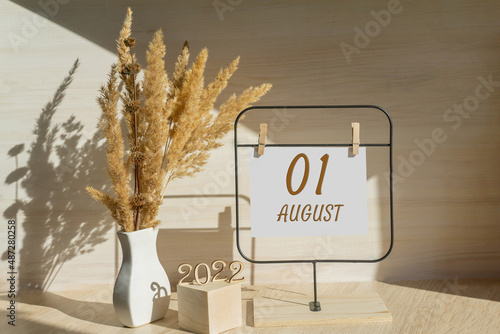 august 1. 1th day of month, calendar date. White vase with dead wood next to the numbers 2022 and stand with an empty sheet of paper on table. Concept of day of year, time planner, summer month photo