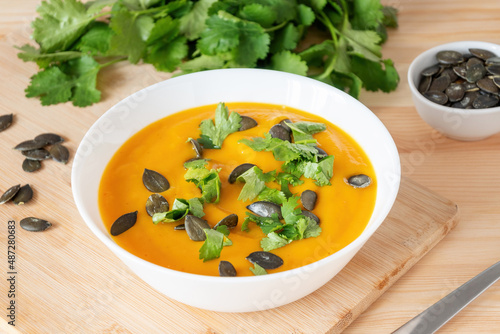 Yellow pumpkin smoothie soup with seeds and green herbs on wooden table. Healthy vegan meal.