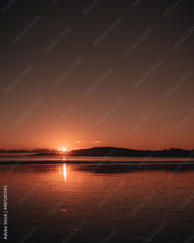 Omaha Beach with a red sunset and reflection on the ocean shore