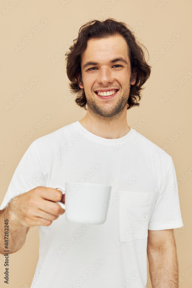 Attractive man with a white mug in his hands emotions posing beige background Attractive man with a white mug in his hands emotions posing beige background