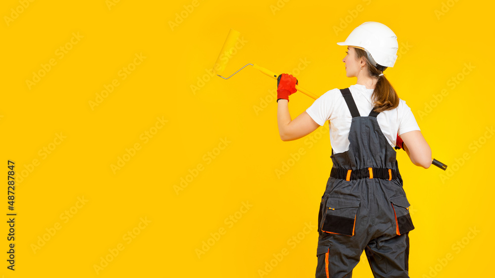 Woman molar with roller in hands. Girl paints empty wall. Woman molar stands with her back to camera. Space for your proposal on yellow. Concept woman draws inscription on wall. Blank for ads banner Woman molar with roller in hands. Girl paints empty wall. Woman molar stands with her back to camera. Space for your proposal on yellow. Concept woman draws inscription on wall. Blank for ads banner