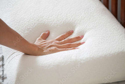woman holding white thin memory foam pillow on white bedsheets