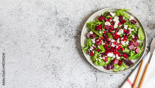 Arugula, Beet and cheese salad with pomegranate and dressing on plate on grey stone kitchen table background, place for text, top view