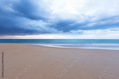 The view of the beach has white foam waves hitting the sand with turquoise water. Fluid dynamics  wave action in low light at sunset