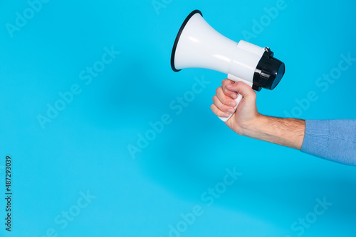 Lifestyle Concepts. Closeup of Hand of Man in Blue Jumper Holding Megaphone Loudspeaker Against Seamless Blue Background.