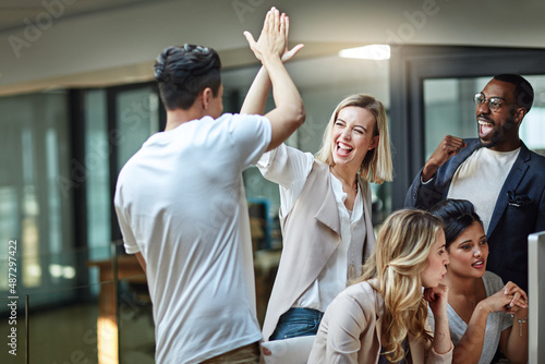 Weve done it again. Shot of a group of colleagues giving each other a high five while using a computer together at work. photo