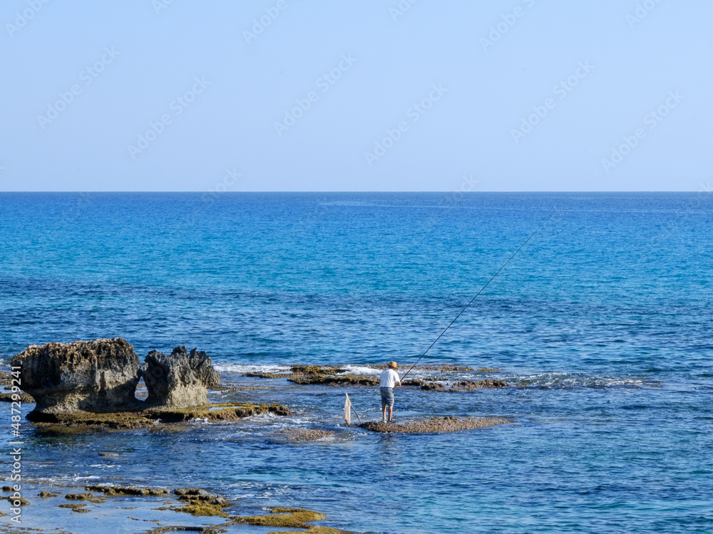 Fototapeta premium fisherman catches fish on the rocky seashore