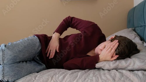 Stressed young woman lying on bed, embracing belly, suffering from stomachache or menstrual painful feelings. Gastritis, abdominal or period pain concept.