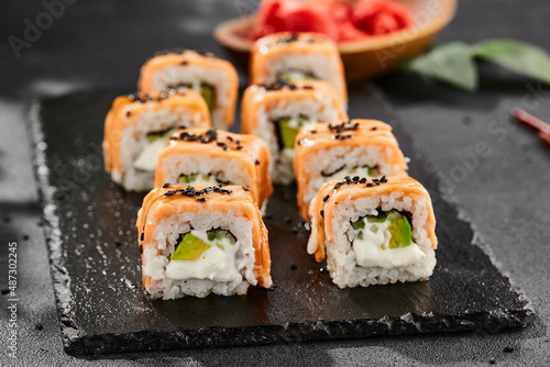 Maki sushi on dark slate. Hot philadelphia maki with baked salmon. Sushi roll with grilled salmon, cream cheese and avocado. Style concept japanese menu with black background, leaves and hard shadow.