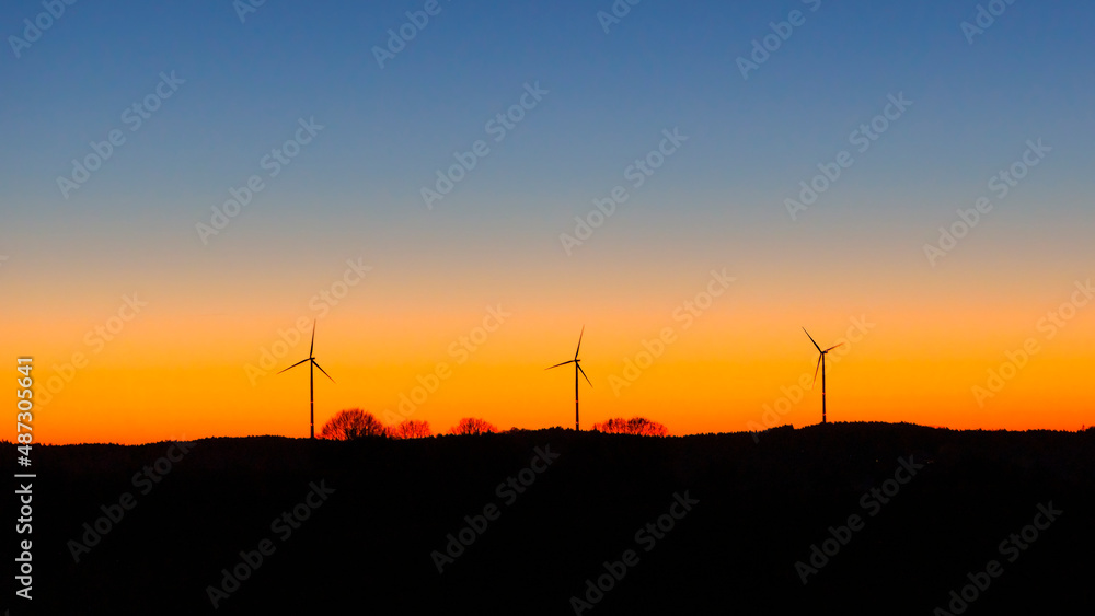 Silhouettes of three wind turbines against a magnificent colored evening sky with cloudless sky in the evening