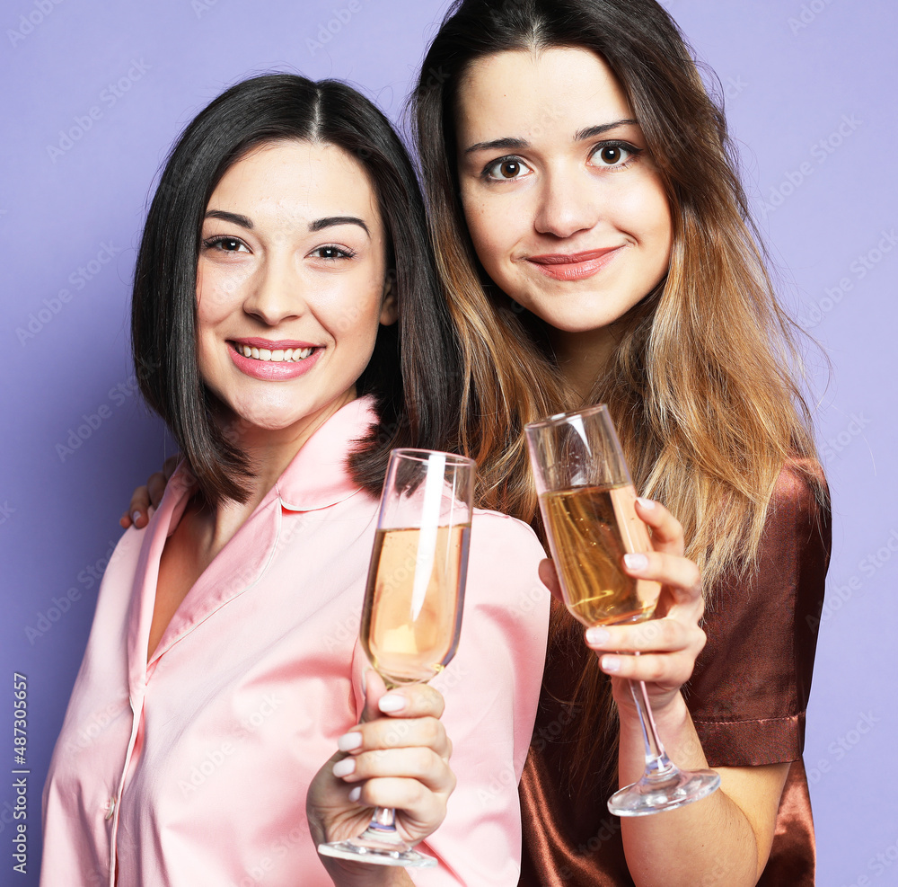 two beautiful women dressed in pajamas drink champagne over purple background two beautiful women dressed in pajamas drink champagne over purple background