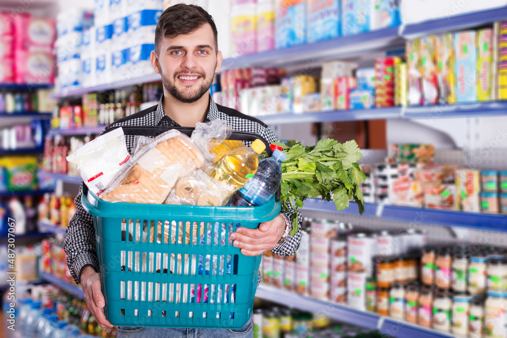 young man with variety of products in shopping basket in store