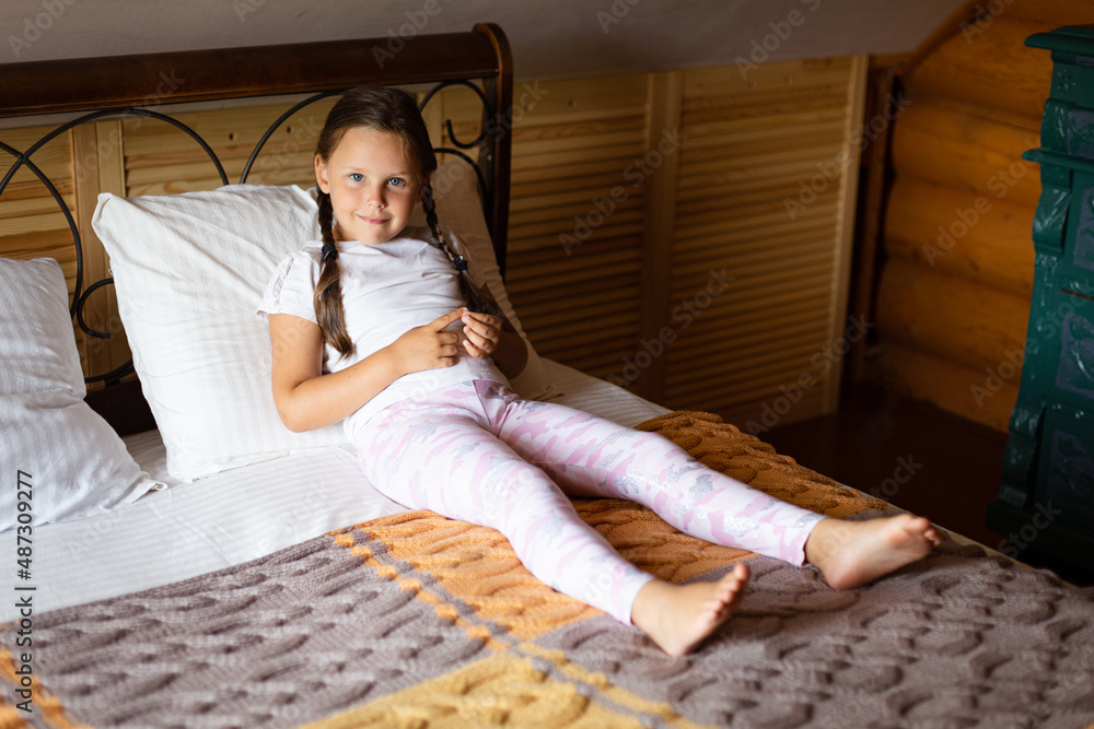 Young girl lying on large double bed covered with gray yellow blanket