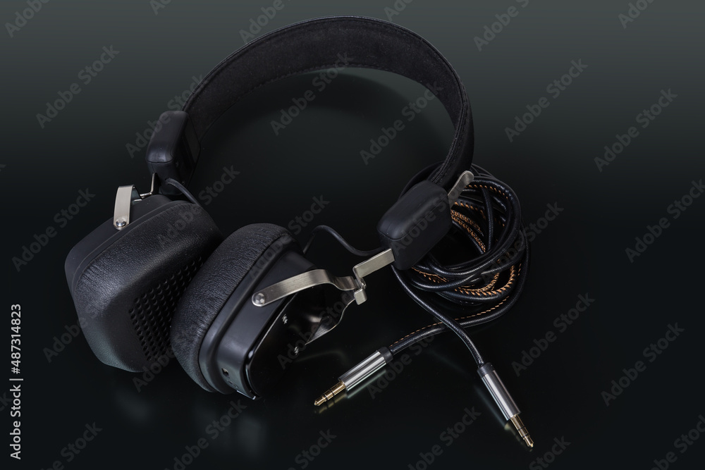 Black ear speakers and audio cable on a dark surface Black ear speakers and audio cable on a dark surface