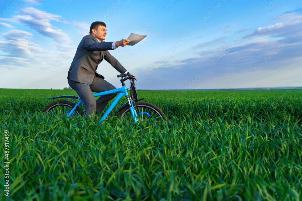 businessman dressed in a business suit, rides a bicycle through a green grass field, he has a briefcase and documents, beautiful nature in spring, business concept businessman dressed in a business suit, rides a bicycle through a green grass field, he has a briefcase and documents, beautiful nature in spring, business concept