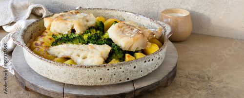 dish with baked potatoes, broccoli and codfish on the table