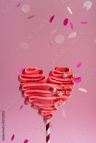 Pink meringue heart on a stick. Pink background, sweets for lovers. Meringue handmade.