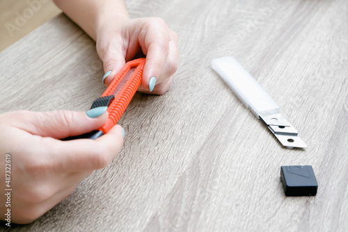 A woman changes a blade in a mounting knife. Hands hold the knife and the new sharp blade. Selective focus. Red plastic knife. photo