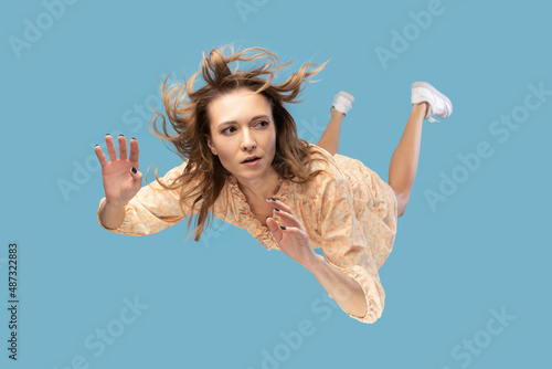 Foto Beautiful young woman levitating in mid-air, falling down and her hair messed up soaring from wind, model flying hovering with dreamy peaceful expression