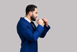 Side view of serious aggressive bearded man holding clenched fists up ready to boxing, defending his rights and freedom, wearing official style suit. Indoor studio shot isolated on gray background.