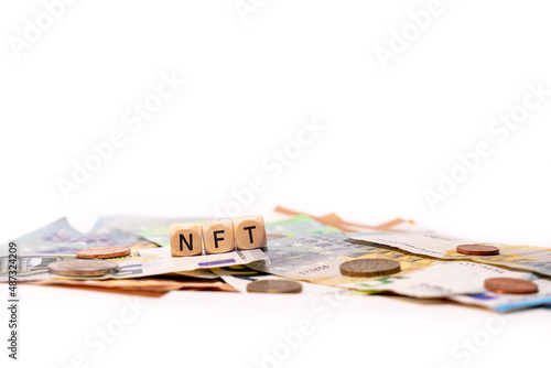 NFT spelled with wooden letters wooden cube on a plain white background with banknotes and coins, concept image photo