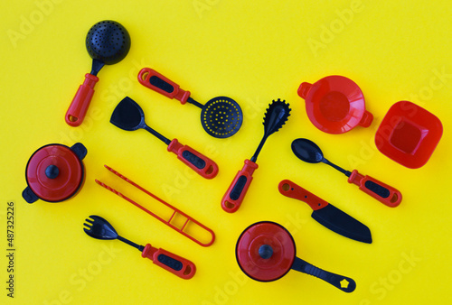 Creative composition of set of children's plastic tableware in red on a yellow background, top view.