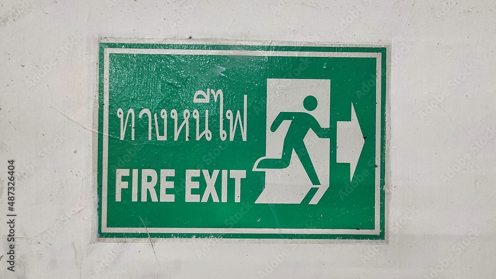 green fire exit sign using English and Thailand language stick on the white wall green fire exit sign using English and Thailand language stick on the white wall