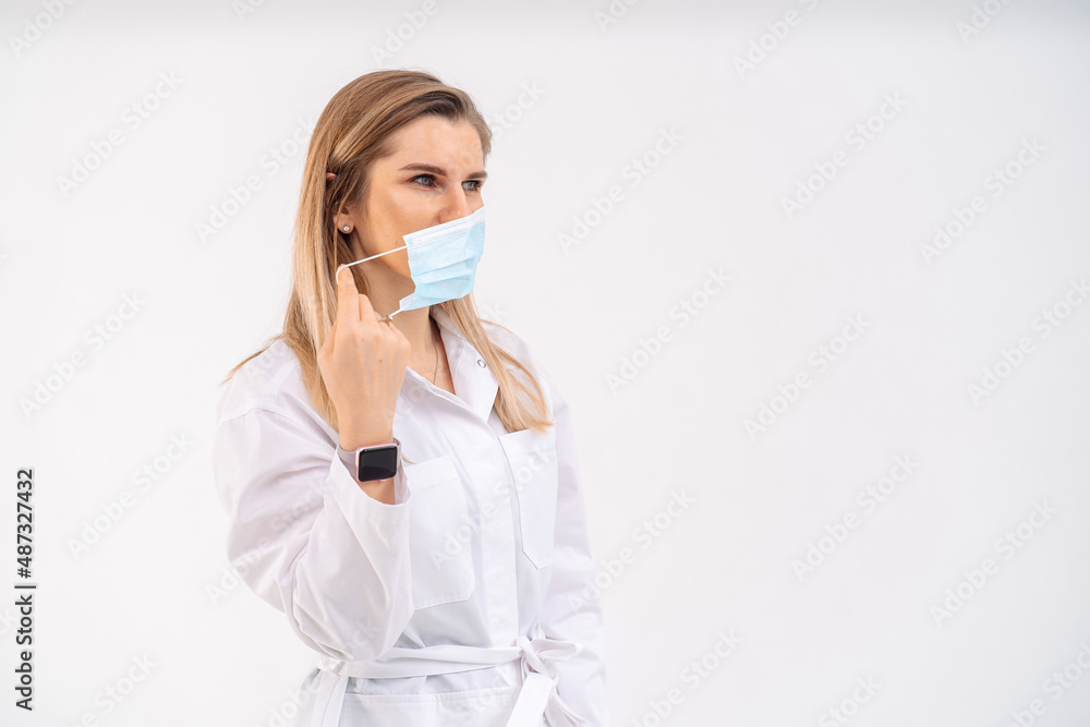 The girl doctor in a white medical gown bactericidal removes the mask on a white background in the hospital.