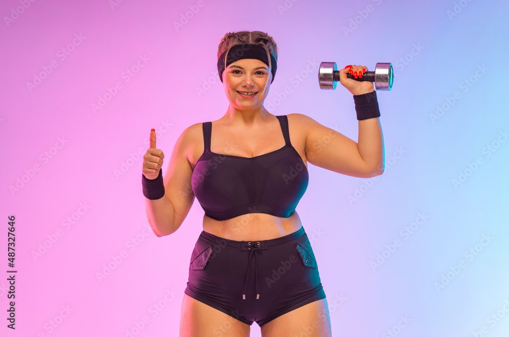 Young fat woman sportswoman. Body positive fitness. The girl wants to lose weight with dumbbells. Girl showing or pointing on copyspace . Young fat woman sportswoman. Body positive fitness. The girl wants to lose weight with dumbbells. Girl showing or pointing on copyspace .