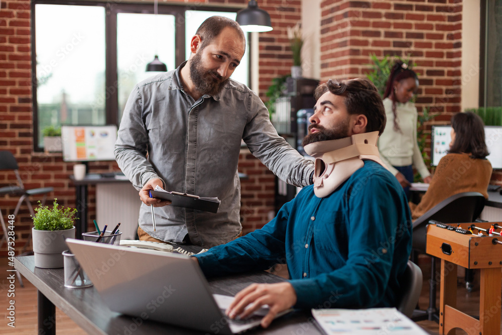 Injured entrepreneur suffering accident having neck pain wearing medical neck collar while working in brick wall startup office. Businessmen analyzing company turnover discussing business strategy