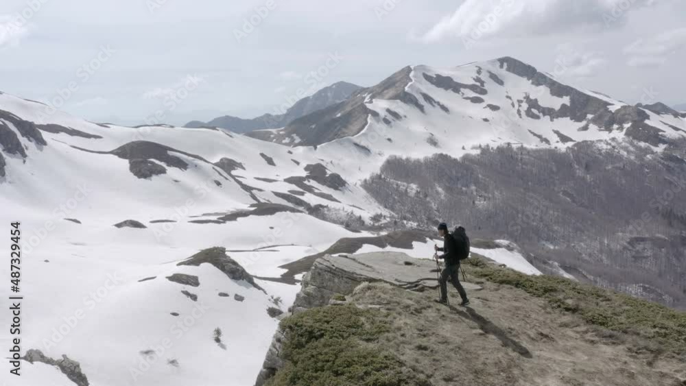 Hiker reaching the top of mountain peak surrounded by mountains covered in snow Hiker reaching the top of mountain peak surrounded by mountains covered in snow