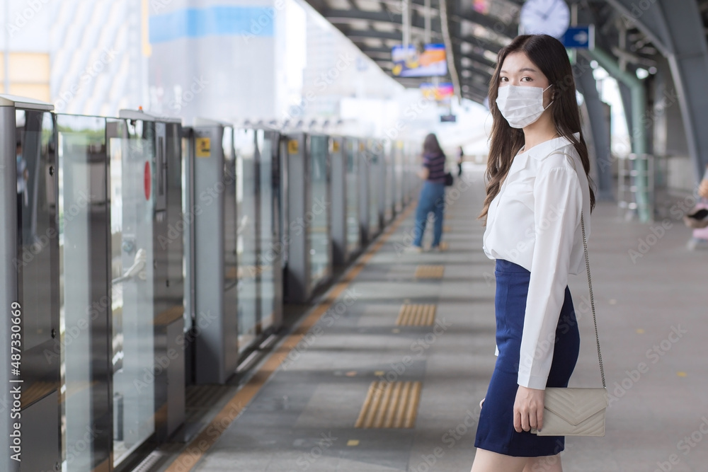Asian business professional woman with long hair wears a mask is waiting to go to workplace or office by sky train in the New Normal lifestyle. Asian business professional woman with long hair wears a mask is waiting to go to workplace or office by sky train in the New Normal lifestyle.