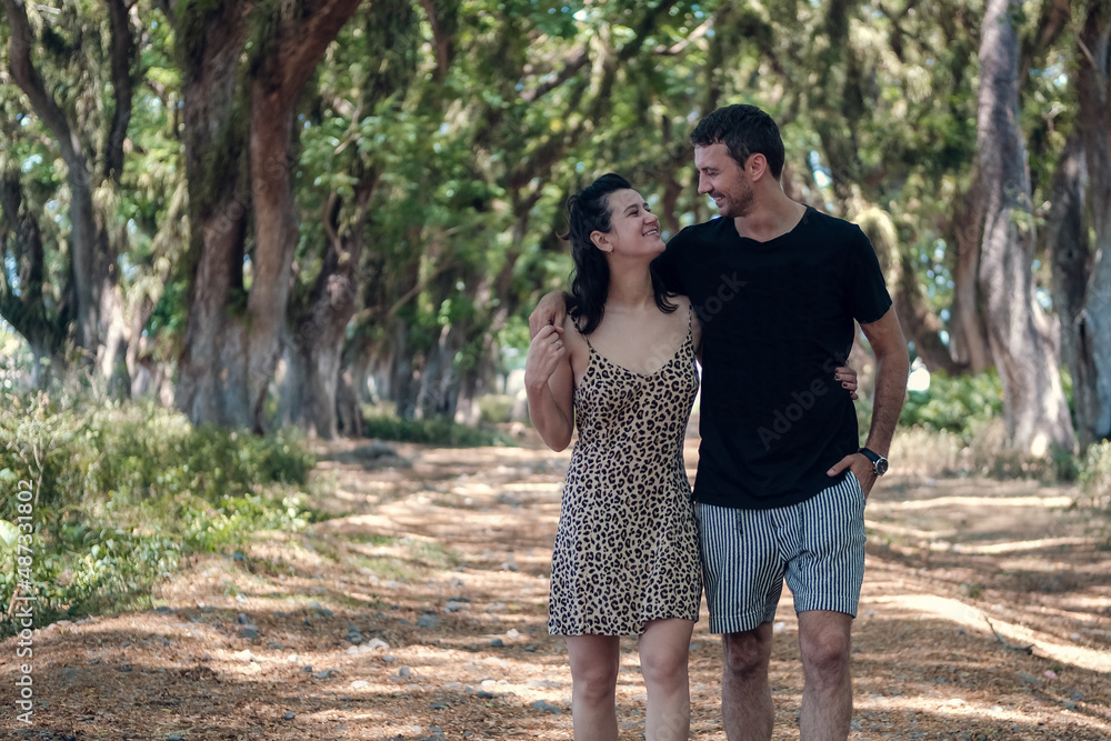 Young couple walking on the walkway lane path with green trees tunnel in the forest or park Young couple walking on the walkway lane path with green trees tunnel in the forest or park